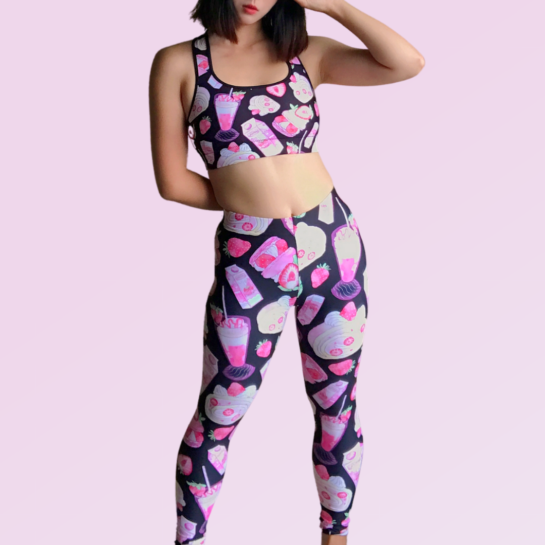 Trendy woman in colorful leggings and sports bra featuring playful dessert prints on a light pink background.